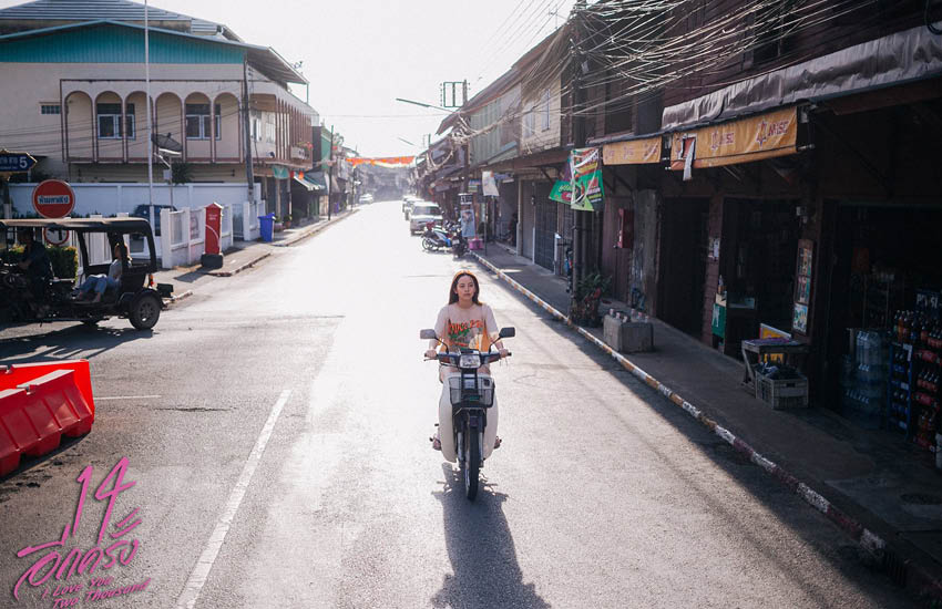 ผู้หญิงขับมอเตอร์ไซค์บนถนนโล่ง ในซอยบ้านเก่า