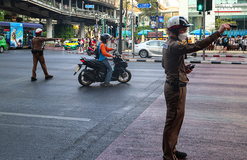 ตำรวจจราจรใช้ไฟฉายส่องเตือนผู้ขับขี่ที่จอดรถทับทางม้าลายบริเวณแยกราชประสงค์