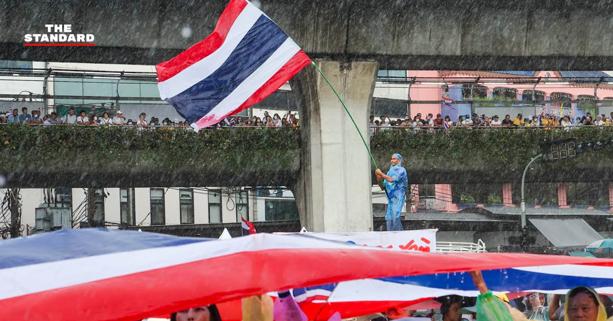 ผู้ชุมนุมม็อบอนุสาวรีย์ชัยถือธงชาติไทยท่ามกลางฝนตกหนัก ขณะฟังการปราศรัยบนเวที
