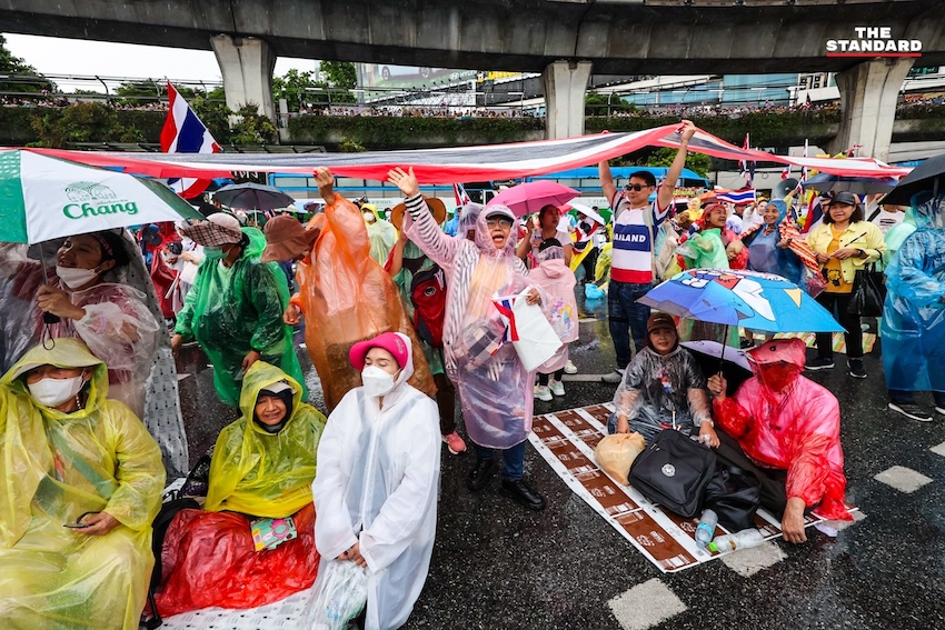 ผู้ชุมนุมม็อบอนุสาวรีย์ชัยถือธงชาติไทยท่ามกลางฝนตกหนัก ขณะฟังการปราศรัยบนเวที