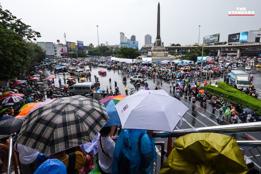 ผู้ชุมนุมม็อบอนุสาวรีย์ชัยถือธงชาติไทยท่ามกลางฝนตกหนัก ขณะฟังการปราศรัยบนเวที