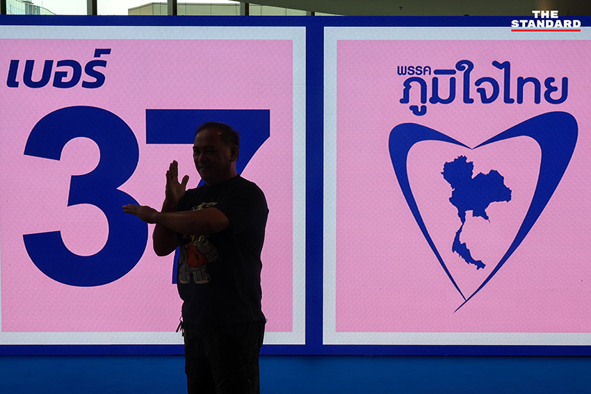 ประชาชนสวมเสื้อสีน้ำเงินร่วมฟังปราศรัยใหญ่พรรคภูมิใจไทย พร้อมถ่ายรูปกับป้ายนโยบายและภาพแกนนำ 1