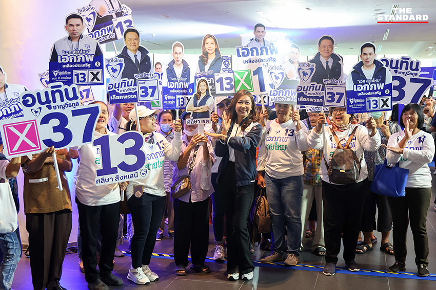 ประชาชนสวมเสื้อสีน้ำเงินร่วมฟังปราศรัยใหญ่พรรคภูมิใจไทย พร้อมถ่ายรูปกับป้ายนโยบายและภาพแกนนำ 9