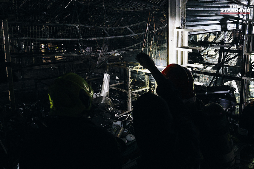 ภาพมุมกว้างเหตุเพลิงไหม้ร้านค้าในตลาดนัดจตุจักรยามค่ำคืน ขณะเจ้าหน้าที่ระดมกำลังฉีดน้ำสกัดเพลิง โดยมีควันไฟพวยพุ่งเหนือหลังคา 12