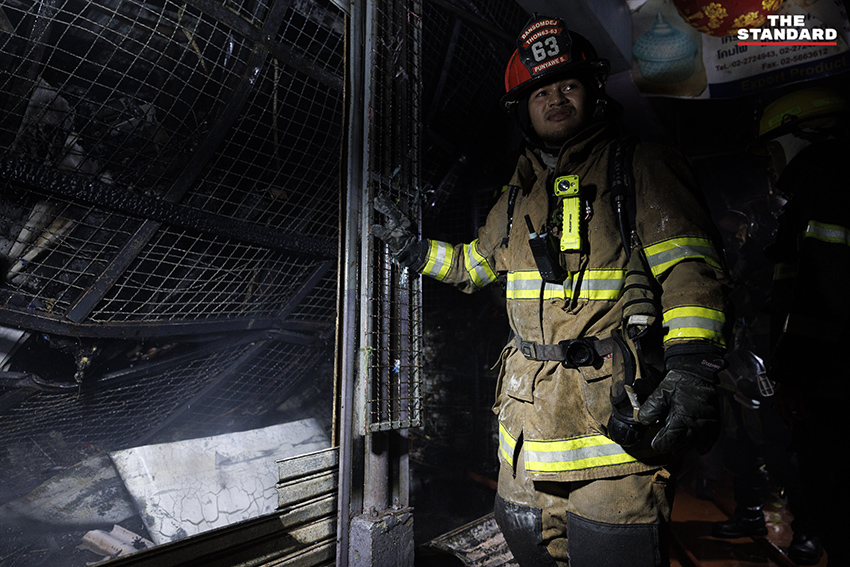 ภาพมุมกว้างเหตุเพลิงไหม้ร้านค้าในตลาดนัดจตุจักรยามค่ำคืน ขณะเจ้าหน้าที่ระดมกำลังฉีดน้ำสกัดเพลิง โดยมีควันไฟพวยพุ่งเหนือหลังคา 13