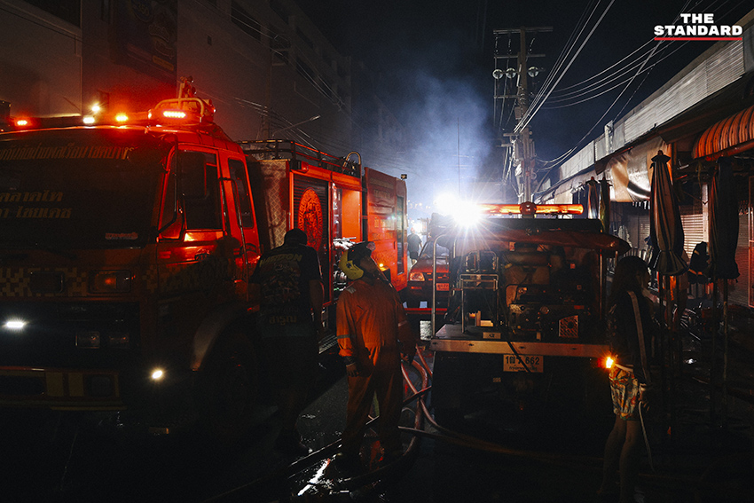 ภาพมุมกว้างเหตุเพลิงไหม้ร้านค้าในตลาดนัดจตุจักรยามค่ำคืน ขณะเจ้าหน้าที่ระดมกำลังฉีดน้ำสกัดเพลิง โดยมีควันไฟพวยพุ่งเหนือหลังคา 2