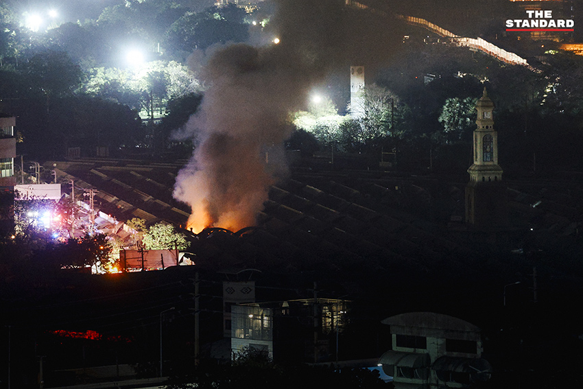 ภาพมุมกว้างเหตุเพลิงไหม้ร้านค้าในตลาดนัดจตุจักรยามค่ำคืน ขณะเจ้าหน้าที่ระดมกำลังฉีดน้ำสกัดเพลิง โดยมีควันไฟพวยพุ่งเหนือหลังคา 4