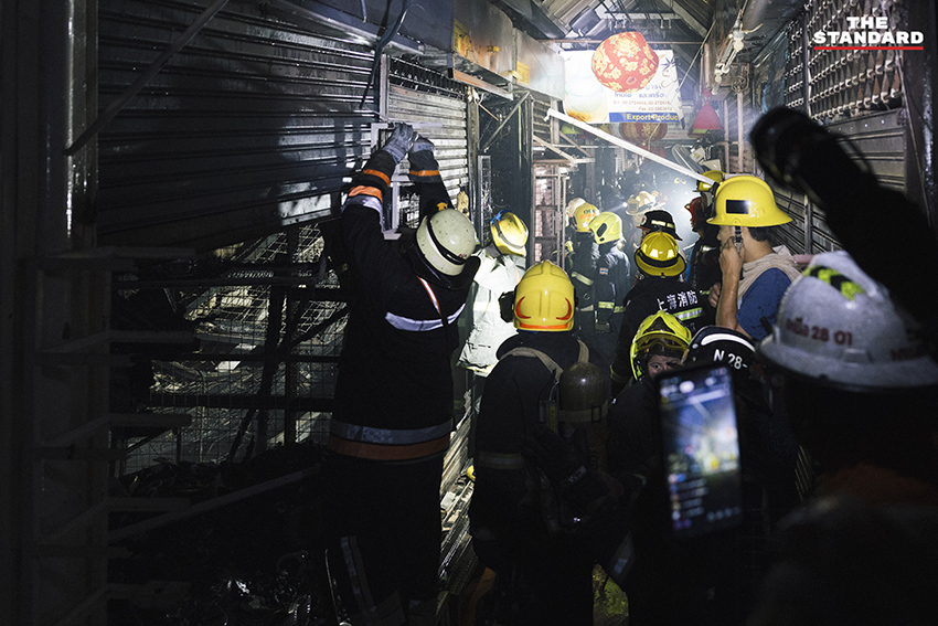 ภาพมุมกว้างเหตุเพลิงไหม้ร้านค้าในตลาดนัดจตุจักรยามค่ำคืน ขณะเจ้าหน้าที่ระดมกำลังฉีดน้ำสกัดเพลิง โดยมีควันไฟพวยพุ่งเหนือหลังคา 5