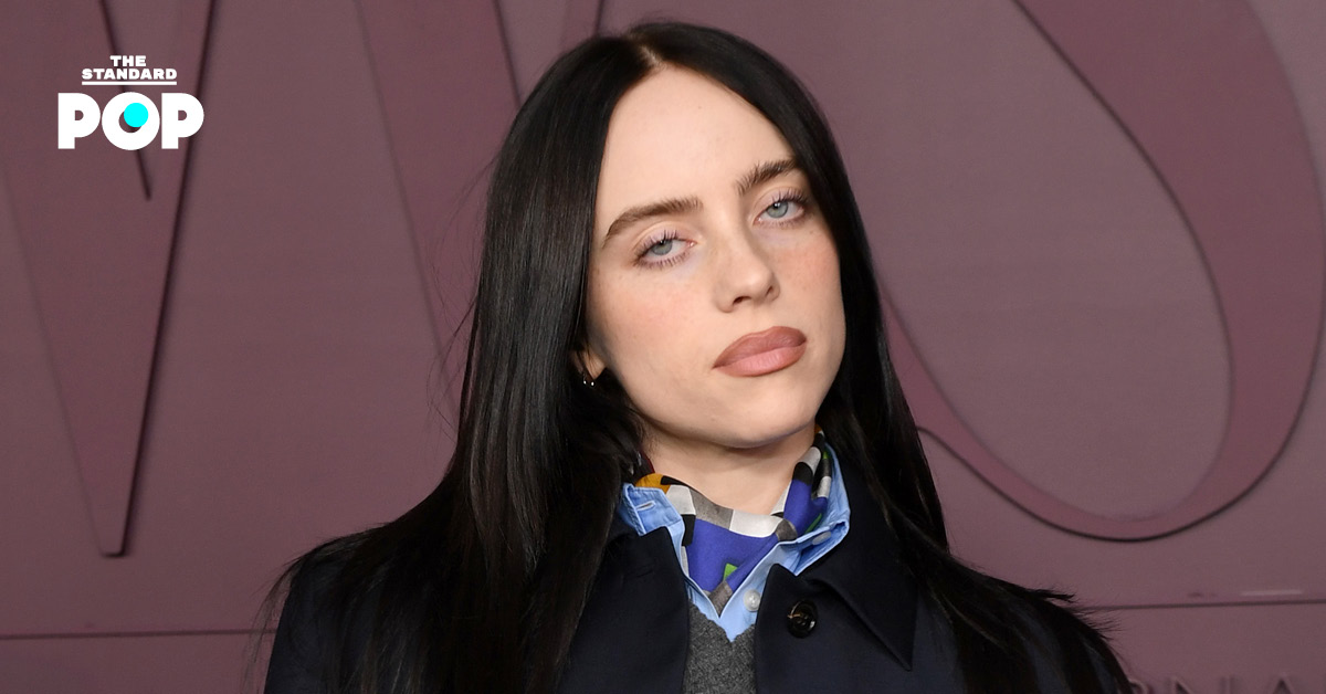 Billie Eilish ในชุดสีขาวกำลังยืนร้องเพลงบนเวทีคอนเสิร์ต