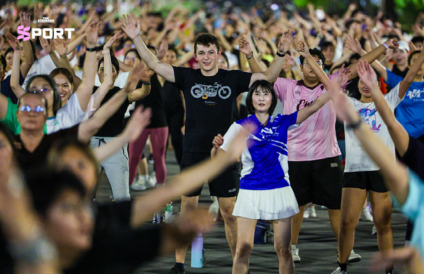 ภาพผู้คนกำลังเต้นแอโรบิกกลางแจ้งที่สวนลุมพินี โดยมีแมวมองดูเป็นกิมมิก 2