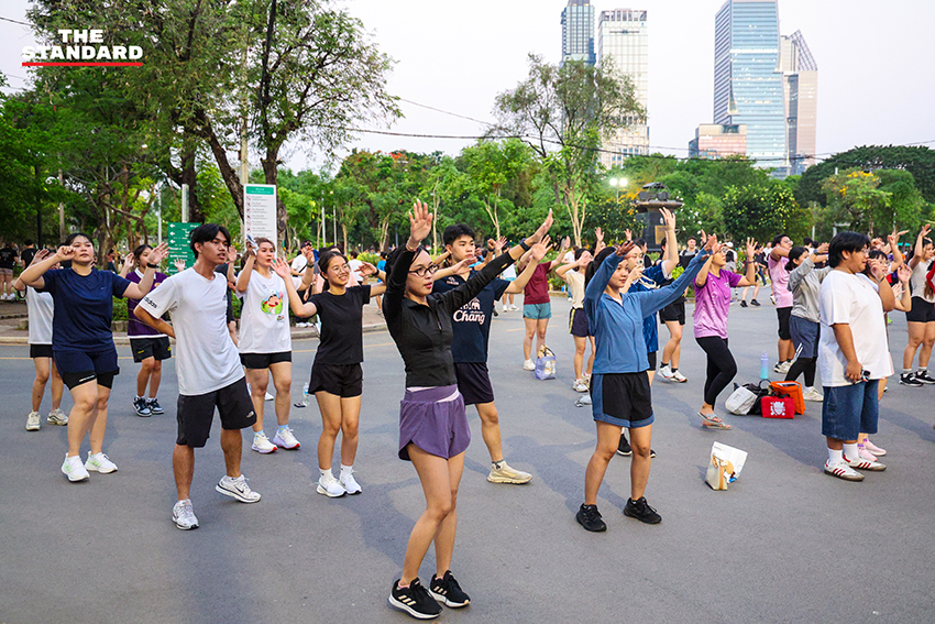 ภาพมุมกว้างของผู้คนจำนวนมากกำลังเต้นแอโรบิกอย่างสนุกสนานที่สวนลุมพินี 13