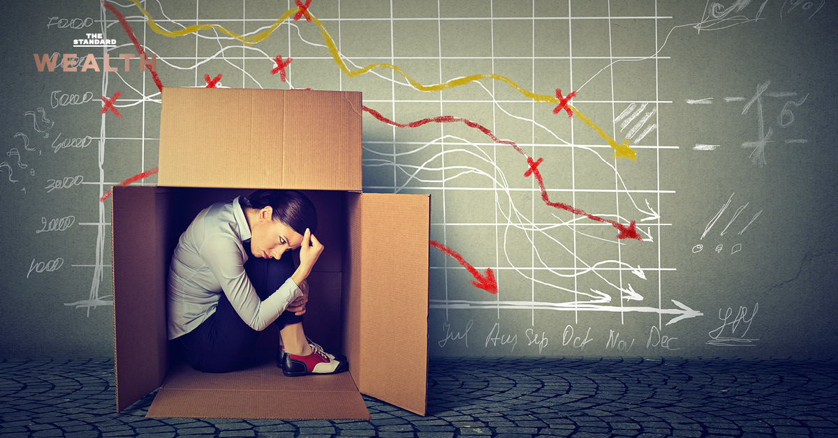 ภาพหญิงสาวท่าทางเครียดเศร้ากำลังนั่งอยู่คนเดียวในกล่อง สื่อถึงความกดดันจากภาวะเศรษฐกิจที่ทรุดตัวและค่าครองชีพสูง