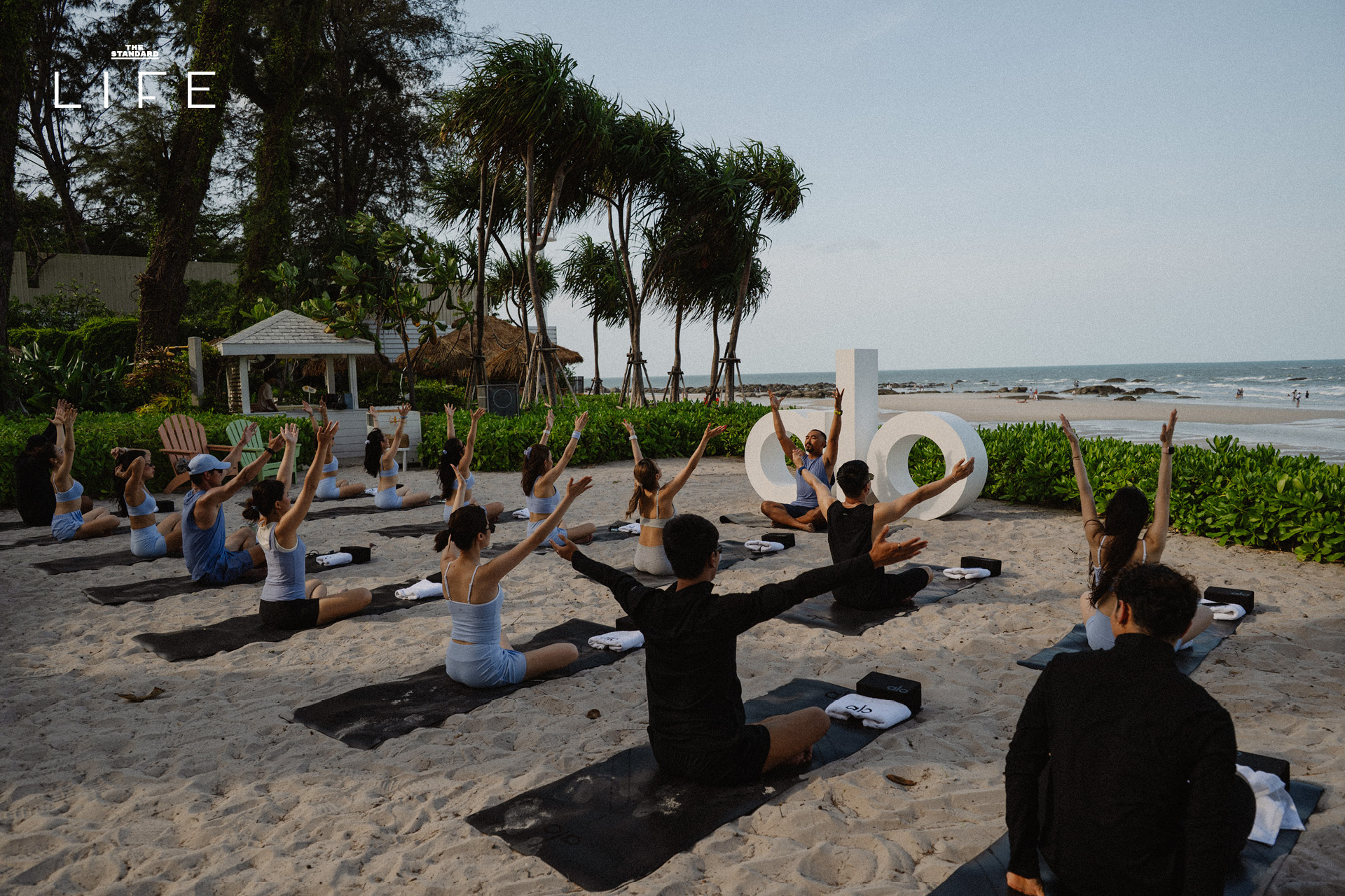 กลุ่มคนกำลังเล่นโยคะริมชายหาดหัวหินในกิจกรรมของ Alo ที่ The Standard, Hua Hin 1