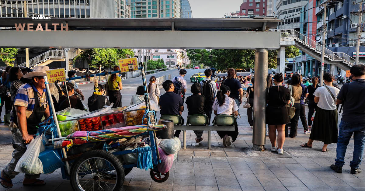 ภาพรถเข็นผลไม้และผู้คนรอรถเมล์ สื่อถึงเศรษฐกิจและชีวิตประจำวันของคนไทย