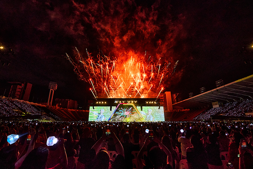 ภาพมุมกว้างของวง TREASURE กำลังแสดงคอนเสิร์ตบนเวทีขนาดใหญ่ท่ามกลางแฟนเพลงและแท่งไฟสีฟ้าเต็มสนามศุภชลาศัย 4