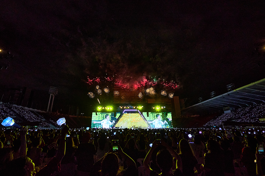 ภาพมุมกว้างของวง TREASURE กำลังแสดงคอนเสิร์ตบนเวทีขนาดใหญ่ท่ามกลางแฟนเพลงและแท่งไฟสีฟ้าเต็มสนามศุภชลาศัย 7