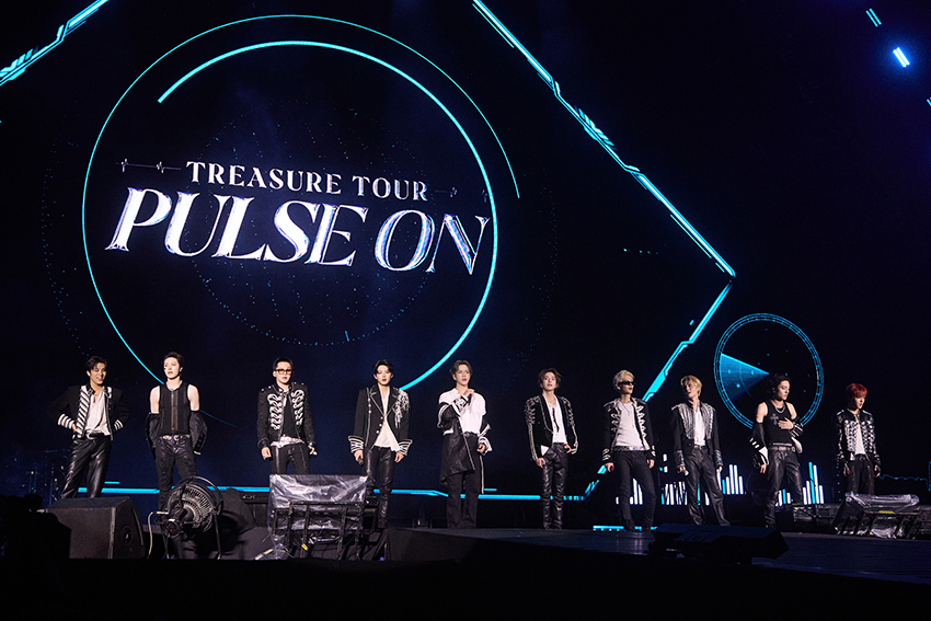 ภาพมุมกว้างของวง TREASURE กำลังแสดงคอนเสิร์ตบนเวทีขนาดใหญ่ท่ามกลางแฟนเพลงและแท่งไฟสีฟ้าเต็มสนามศุภชลาศัย 8