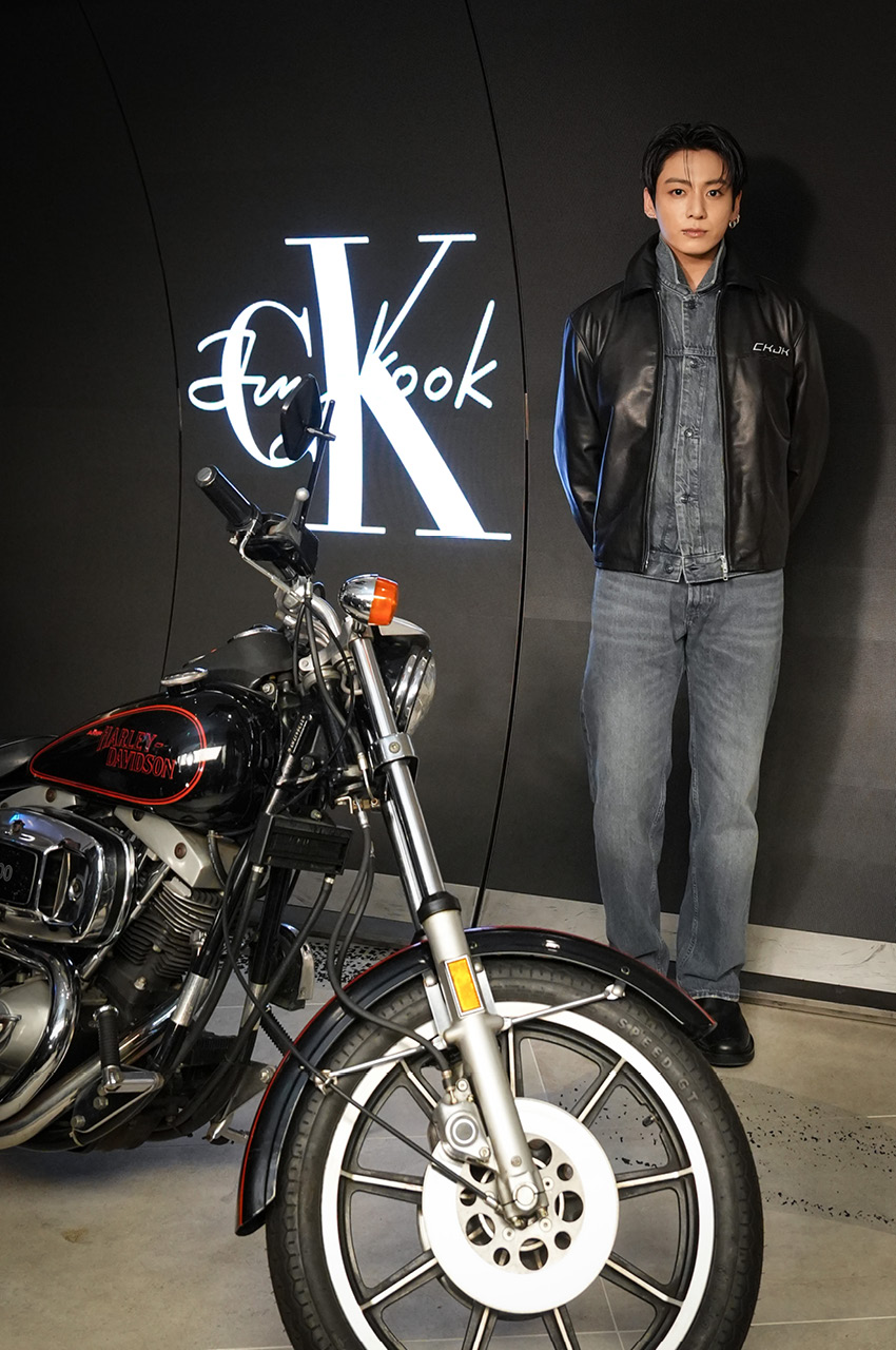 Jung Kook ในชุดแจ็กเกตหนังดีไซน์เรซซิงจาก Calvin Klein ยืนอยู่ภายในงานอีเวนต์ที่แฟล็กชิปสโตร์ฮาราจูกุ 8