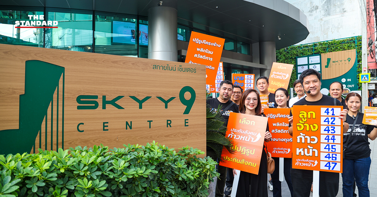 ภาพทีมประกันสังคมก้าวหน้าเดินรณรงค์ถือป้ายหน้าอาคาร SKYY9