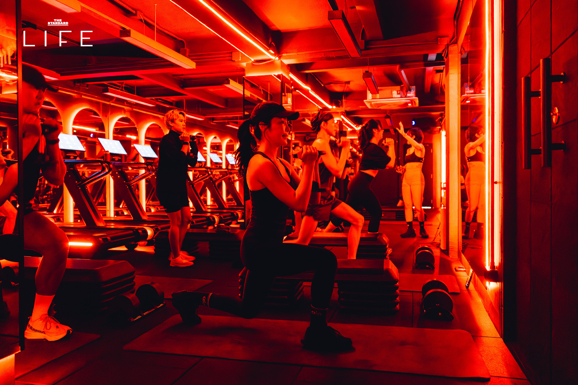 ผู้คนกำลังออกกำลังกายในคลาส HIIT + ASS & ABS ภายในยิม VAULT ที่ตกแต่งด้วยโทนสีแดง 11