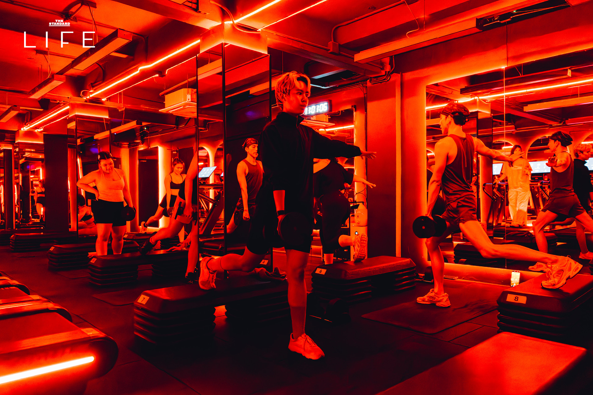 ผู้คนกำลังออกกำลังกายในคลาส HIIT + ASS & ABS ภายในยิม VAULT ที่ตกแต่งด้วยโทนสีแดง 13