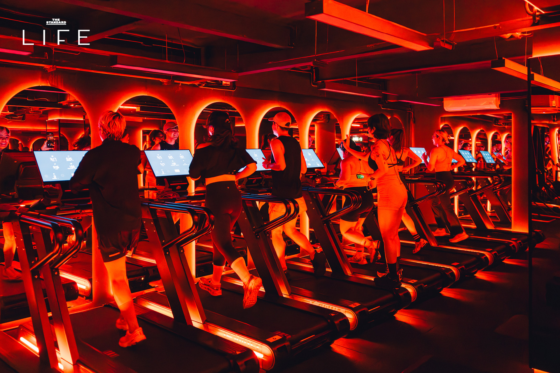 ผู้คนกำลังออกกำลังกายในคลาส HIIT + ASS & ABS ภายในยิม VAULT ที่ตกแต่งด้วยโทนสีแดง 14