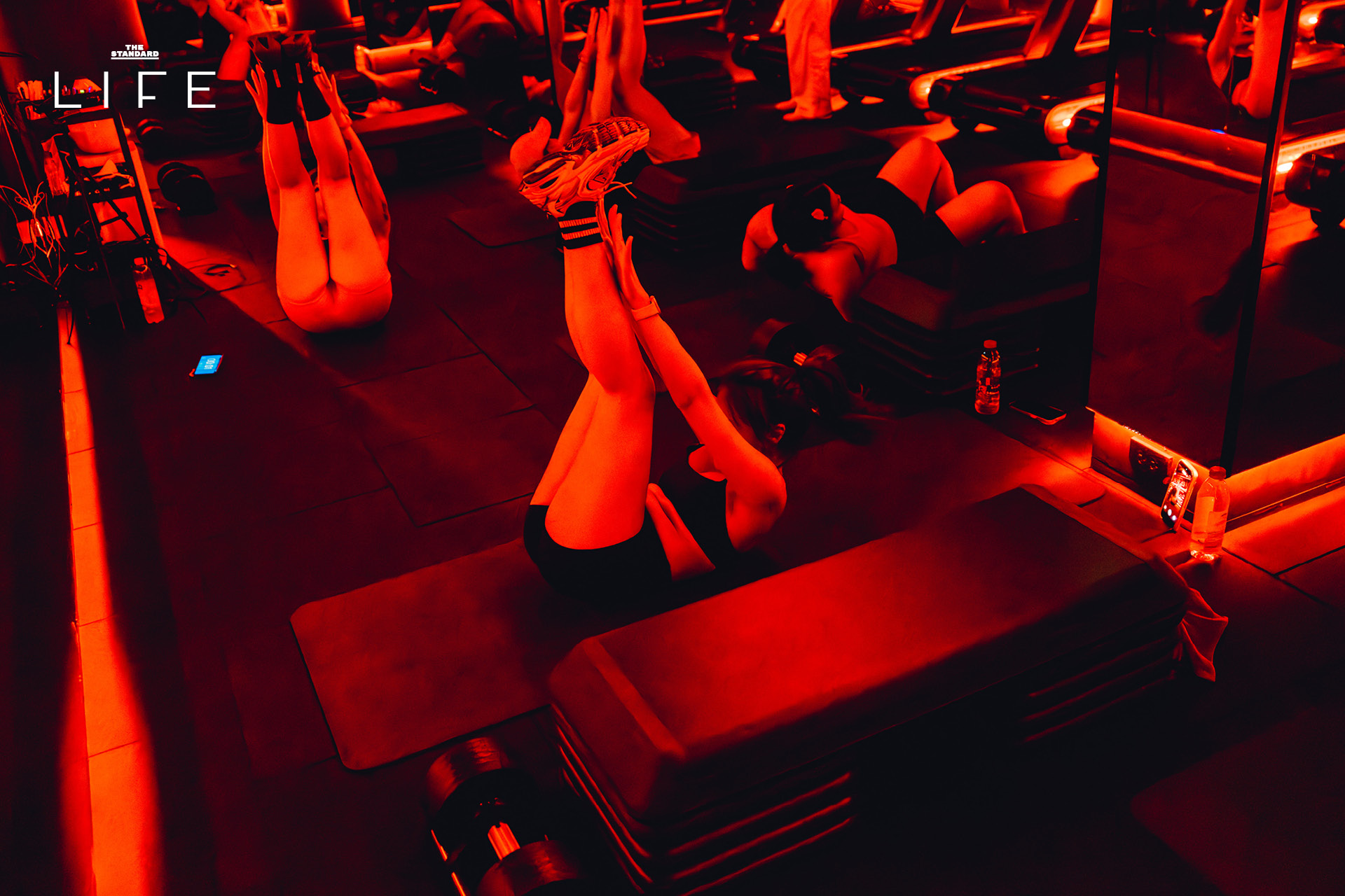 ผู้คนกำลังออกกำลังกายในคลาส HIIT + ASS & ABS ภายในยิม VAULT ที่ตกแต่งด้วยโทนสีแดง 17