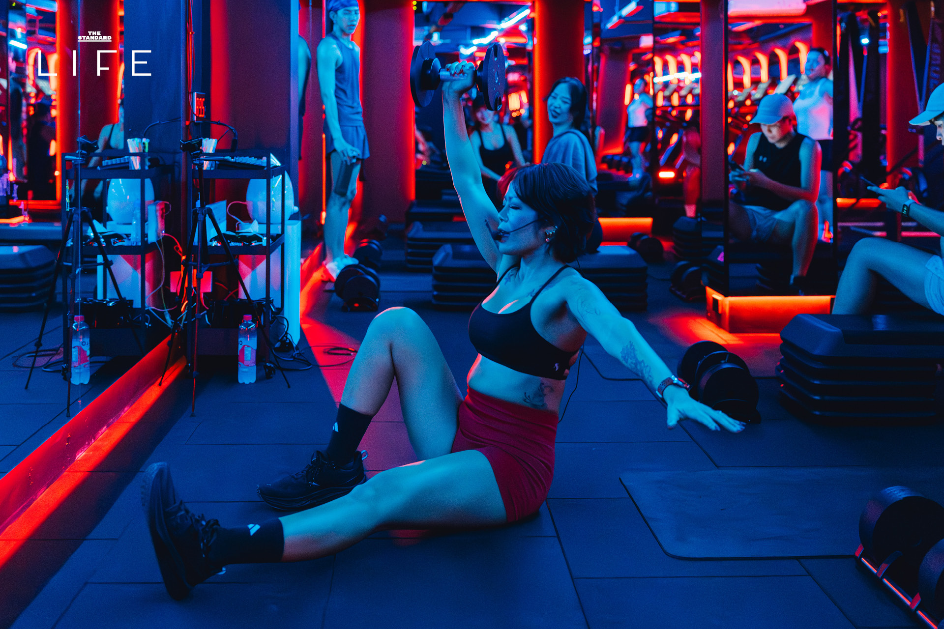 ผู้คนกำลังออกกำลังกายในคลาส HIIT + ASS & ABS ภายในยิม VAULT ที่ตกแต่งด้วยโทนสีแดง 18