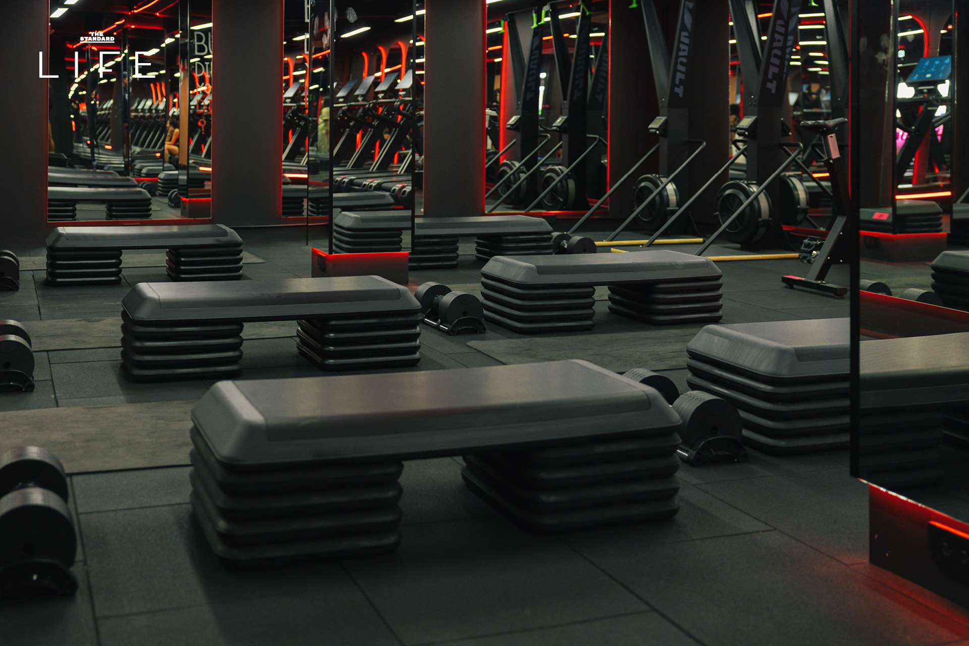 ผู้คนกำลังออกกำลังกายในคลาส HIIT + ASS & ABS ภายในยิม VAULT ที่ตกแต่งด้วยโทนสีแดง 2