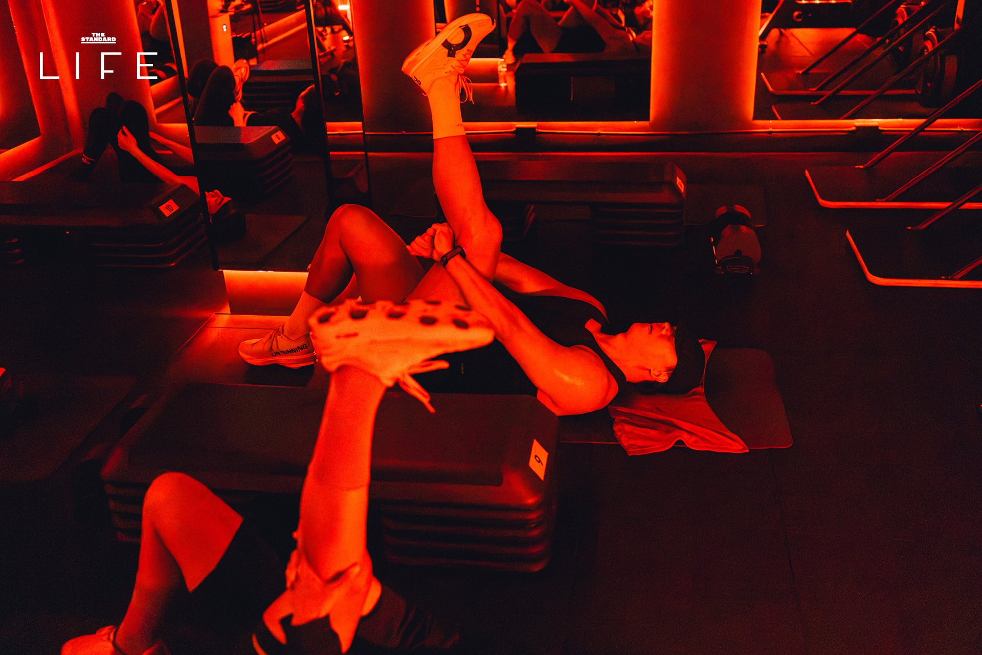 ผู้คนกำลังออกกำลังกายในคลาส HIIT + ASS & ABS ภายในยิม VAULT ที่ตกแต่งด้วยโทนสีแดง 20