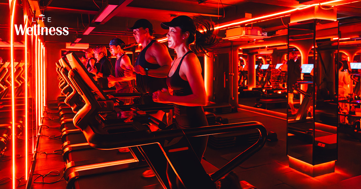 ผู้คนกำลังออกกำลังกายในคลาส HIIT + ASS & ABS ภายในยิม VAULT ที่ตกแต่งด้วยโทนสีแดง
