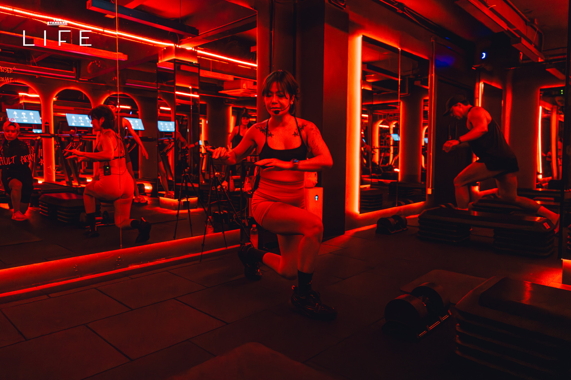 ผู้คนกำลังออกกำลังกายในคลาส HIIT + ASS & ABS ภายในยิม VAULT ที่ตกแต่งด้วยโทนสีแดง 3