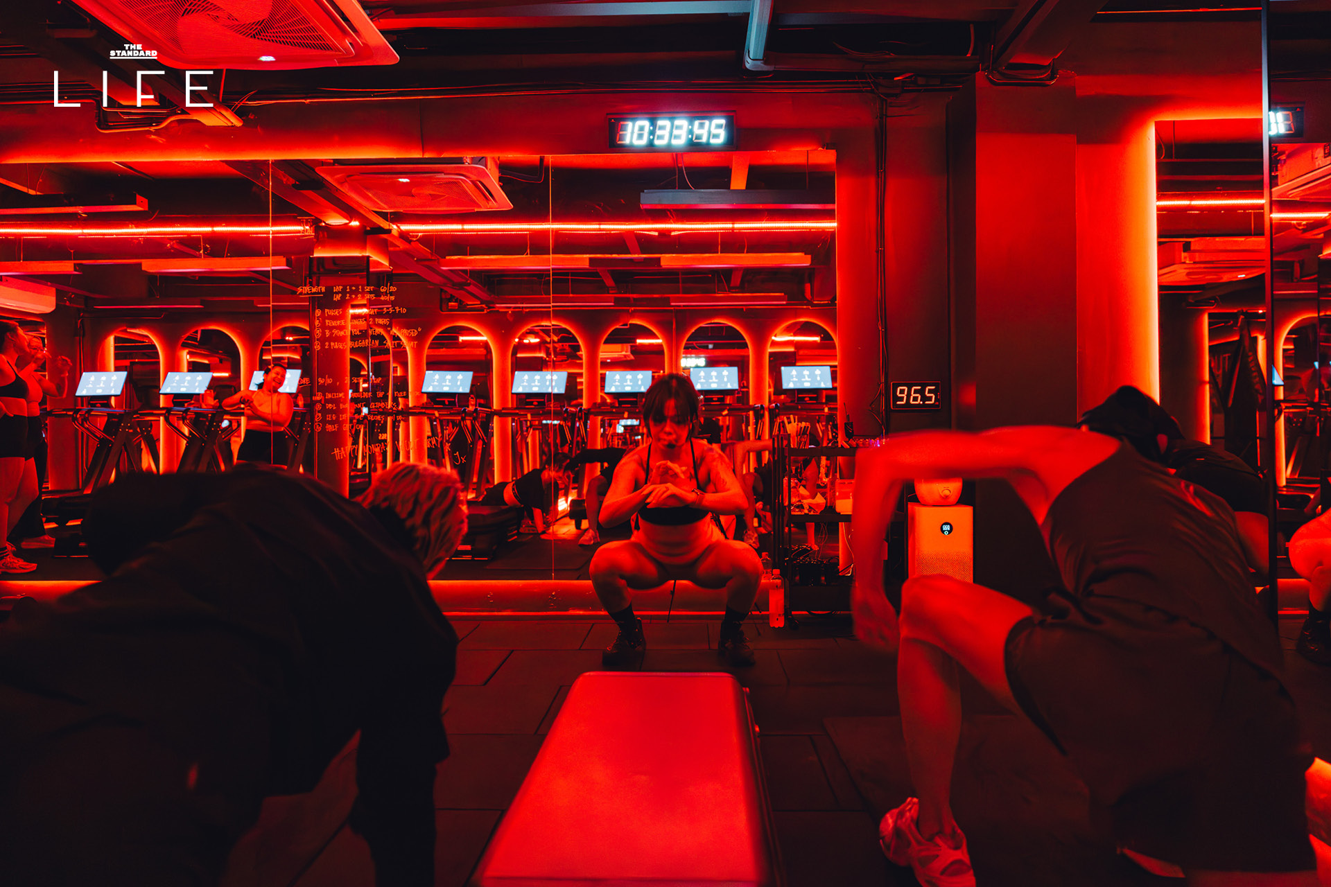 ผู้คนกำลังออกกำลังกายในคลาส HIIT + ASS & ABS ภายในยิม VAULT ที่ตกแต่งด้วยโทนสีแดง 5