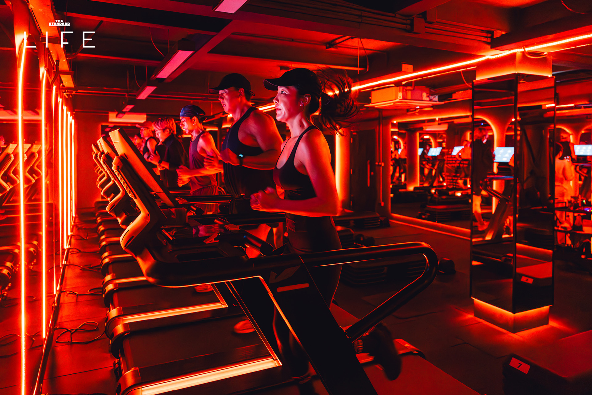 ผู้คนกำลังออกกำลังกายในคลาส HIIT + ASS & ABS ภายในยิม VAULT ที่ตกแต่งด้วยโทนสีแดง 6