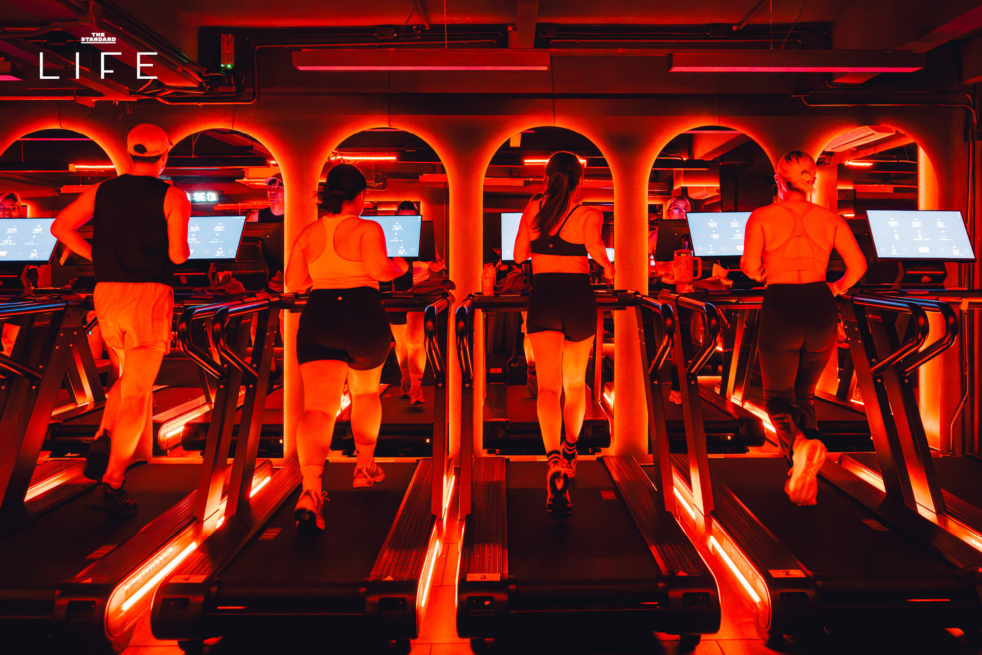 ผู้คนกำลังออกกำลังกายในคลาส HIIT + ASS & ABS ภายในยิม VAULT ที่ตกแต่งด้วยโทนสีแดง 7