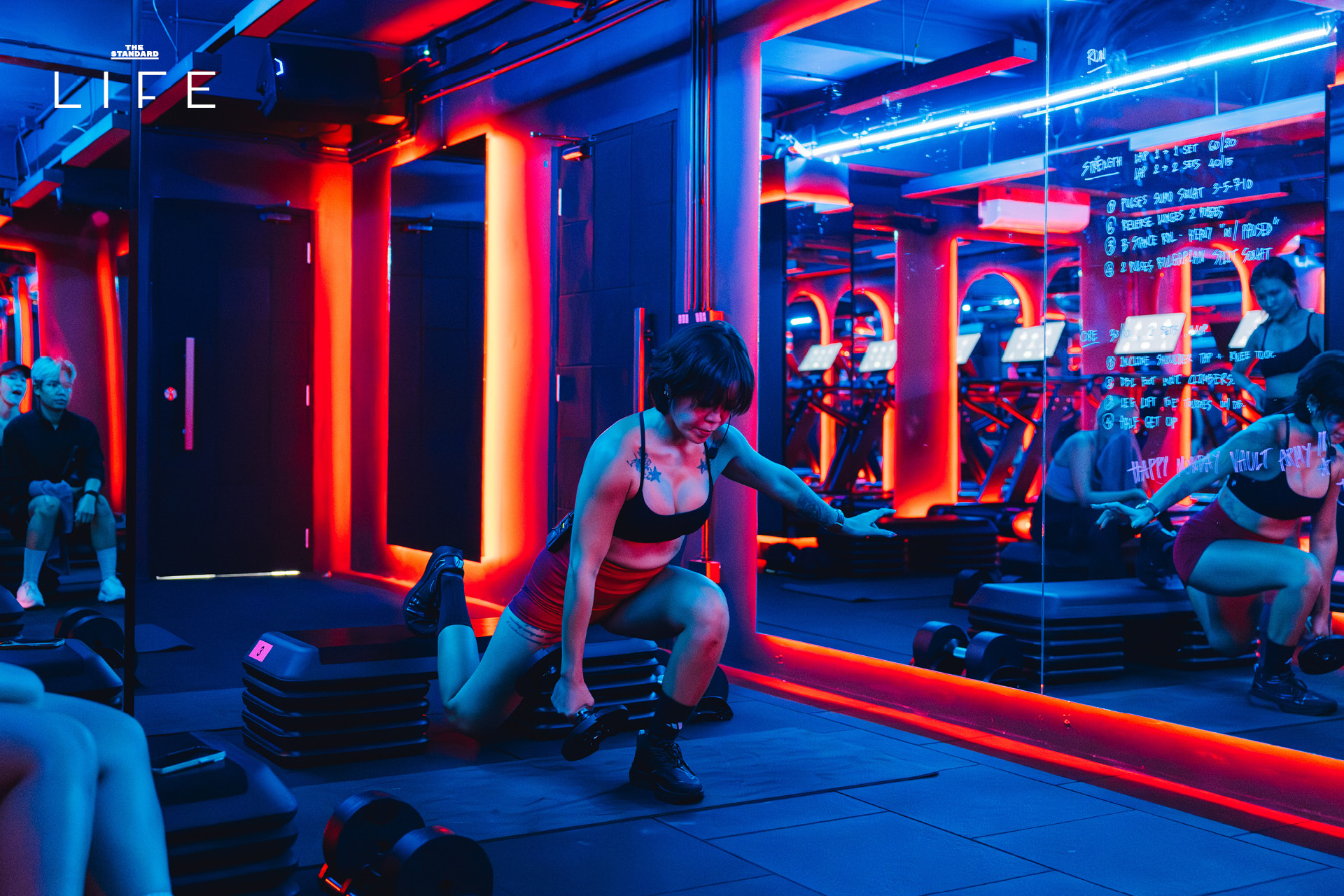 ผู้คนกำลังออกกำลังกายในคลาส HIIT + ASS & ABS ภายในยิม VAULT ที่ตกแต่งด้วยโทนสีแดง 9