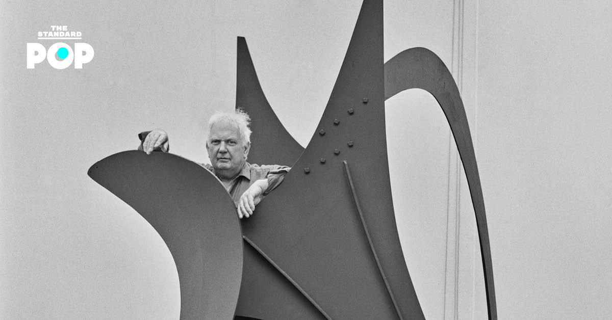 ภาพประติมากร Alexander Calder ยืนอยู่ข้างผลงานโมบายของเขา