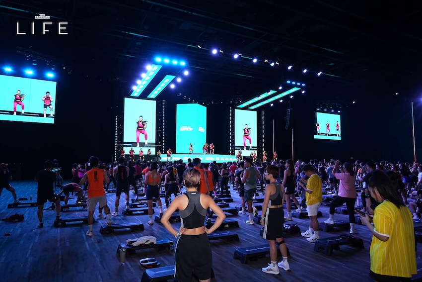 ภาพบรรยากาศงาน LES MILLS LIVE Bangkok 2026 x adidas ที่มีผู้คนจำนวนมากกำลังออกกำลังกายในฮอลล์ขนาดใหญ่ 11