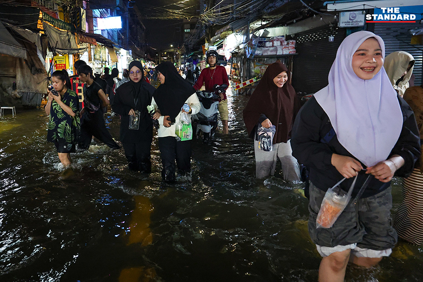 ประชาชนเดินเท้าและใช้รถจักรยานยนต์บนถนนที่มีน้ำท่วมขังบริเวณแยกคลองตัน 1