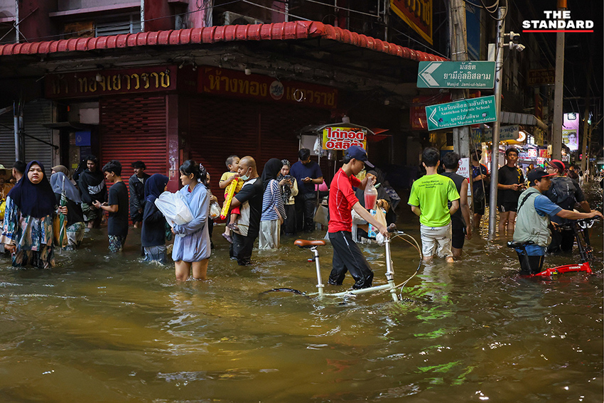 ประชาชนเดินเท้าและใช้รถจักรยานยนต์บนถนนที่มีน้ำท่วมขังบริเวณแยกคลองตัน 13