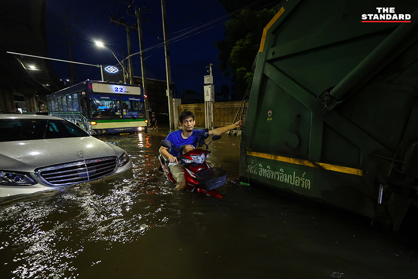 ประชาชนเดินเท้าและใช้รถจักรยานยนต์บนถนนที่มีน้ำท่วมขังบริเวณแยกคลองตัน 14