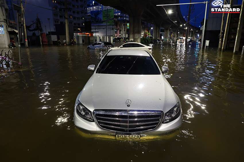 ประชาชนเดินเท้าและใช้รถจักรยานยนต์บนถนนที่มีน้ำท่วมขังบริเวณแยกคลองตัน 16