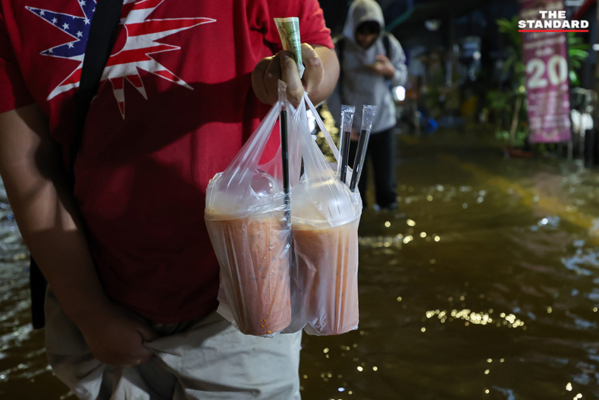 ประชาชนเดินเท้าและใช้รถจักรยานยนต์บนถนนที่มีน้ำท่วมขังบริเวณแยกคลองตัน 2