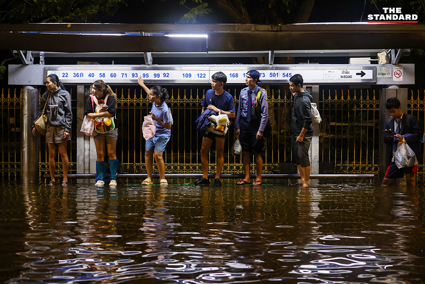ประชาชนเดินเท้าและใช้รถจักรยานยนต์บนถนนที่มีน้ำท่วมขังบริเวณแยกคลองตัน 9